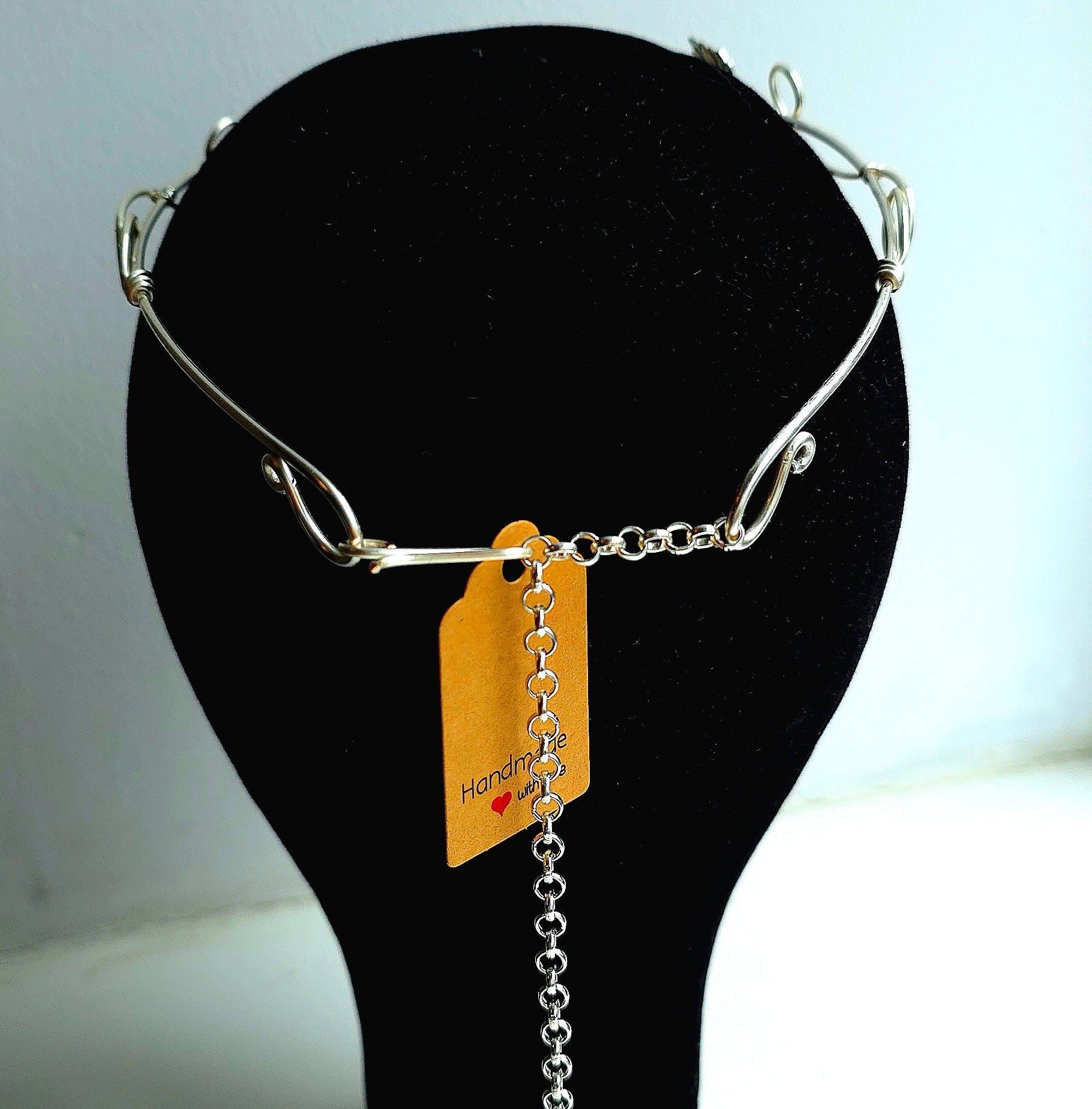 A silver-toned metal necklace displayed on a black mannequin bust, featuring a short chain with a dangling chain link ornament and an orange product tag attached.