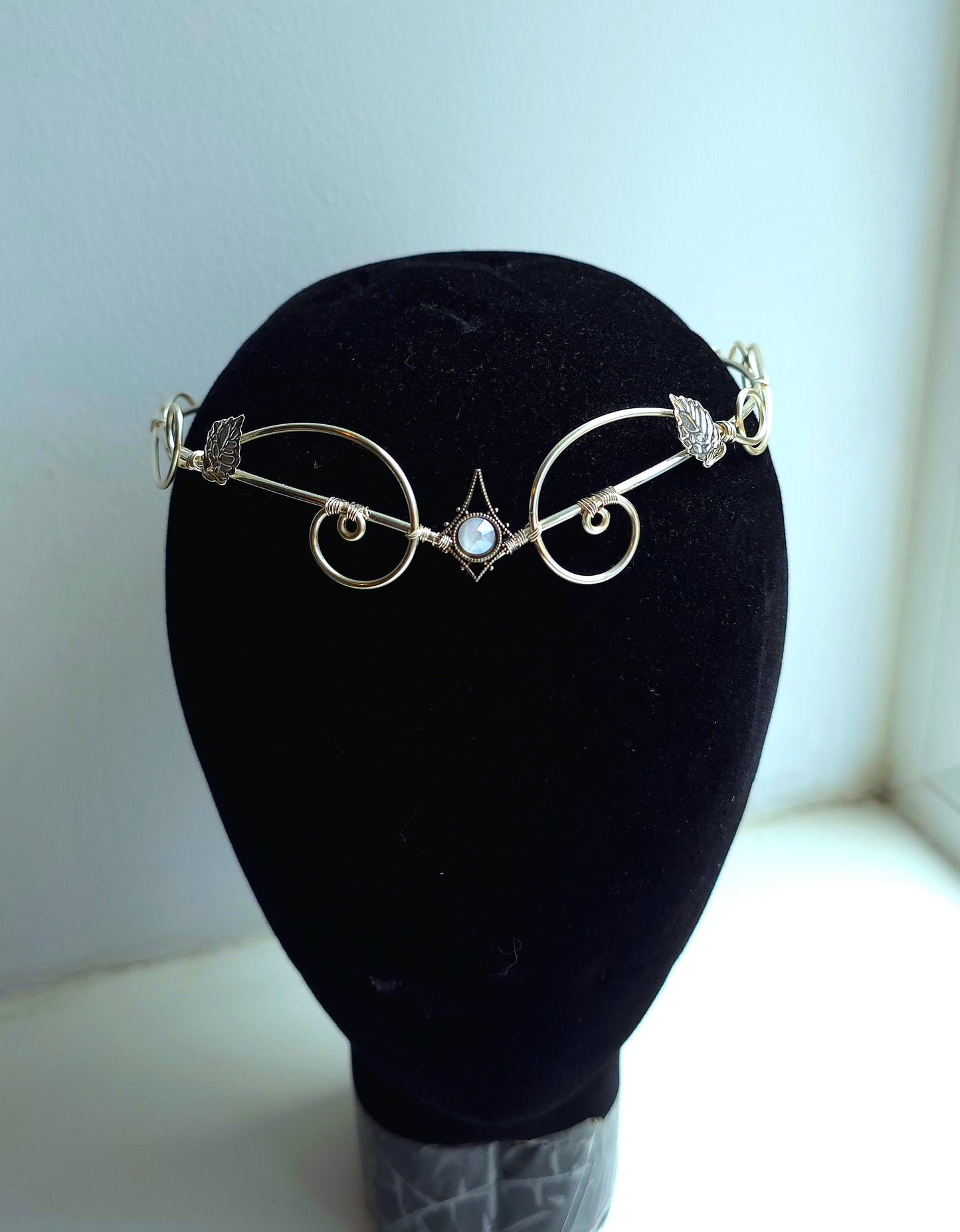 A delicate gold filigree headband with a central white pearl and small clear rhinestone accents, displayed on a black velvet mannequin head.