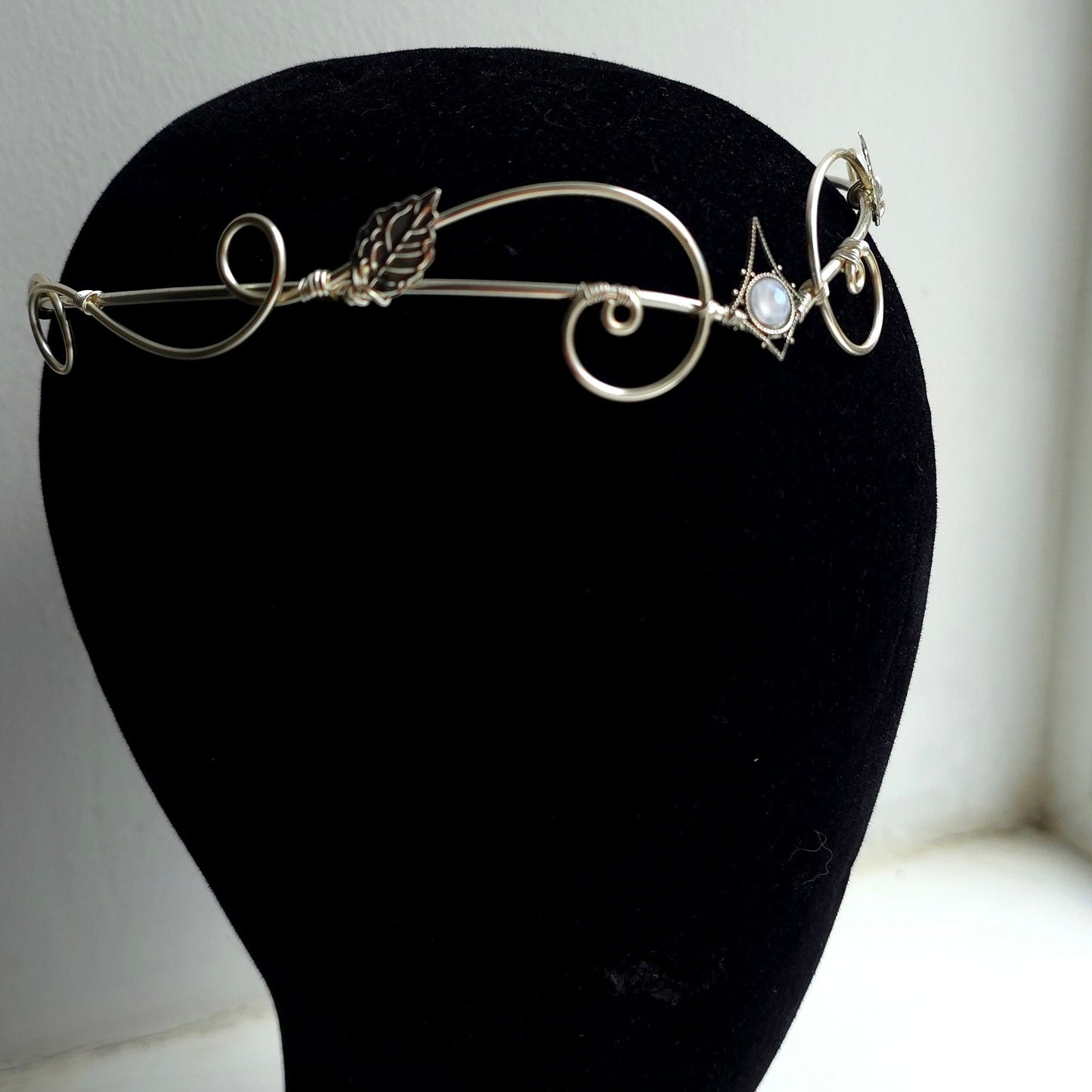A delicate silver filigree tiara with leaf and scroll motifs, displayed on a black velvet mannequin head against a plain white background.