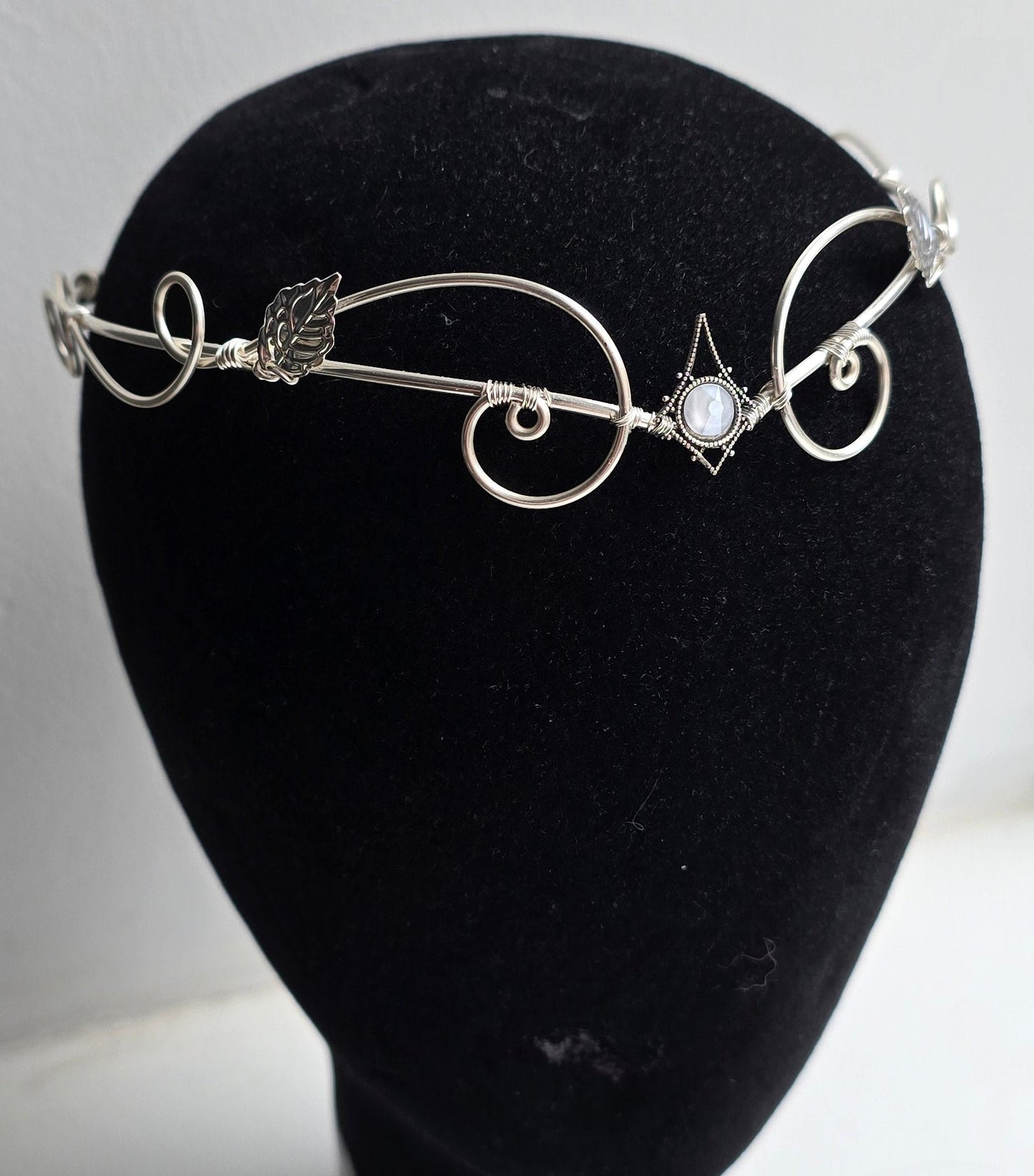 A delicate silver filigree headband with leaf and scroll motifs, displayed on a black velvet mannequin head against a plain white background.