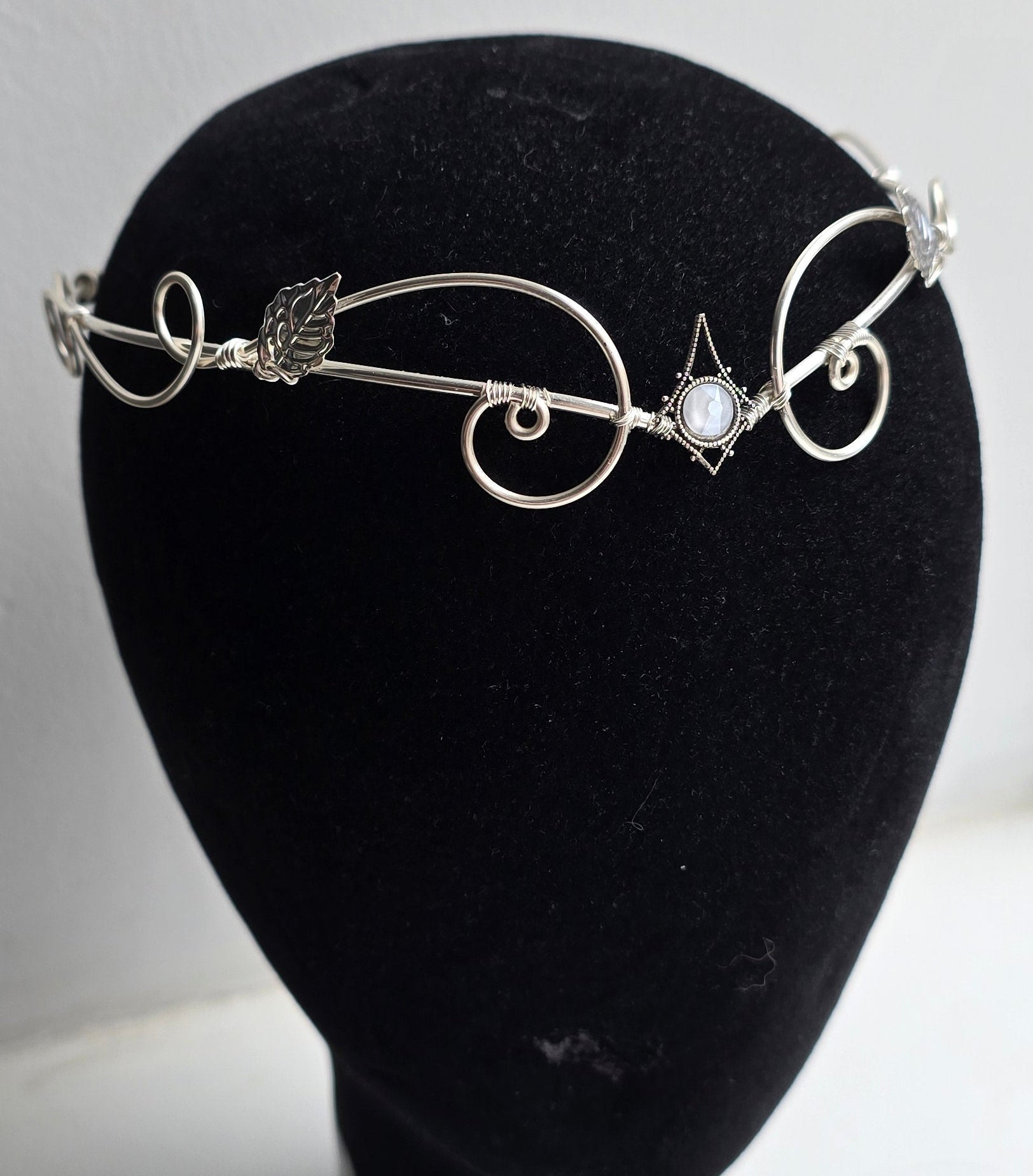A delicate silver filigree headband with leaf and scroll motifs, displayed on a black velvet mannequin head against a plain white background.