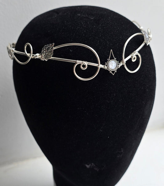 A delicate silver filigree headband with leaf and scroll motifs, displayed on a black velvet mannequin head against a plain white background.
