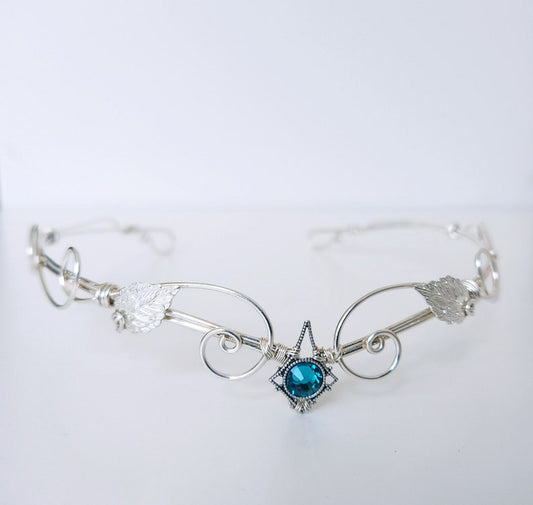 Silver circlet with a blue gemstone on a white background