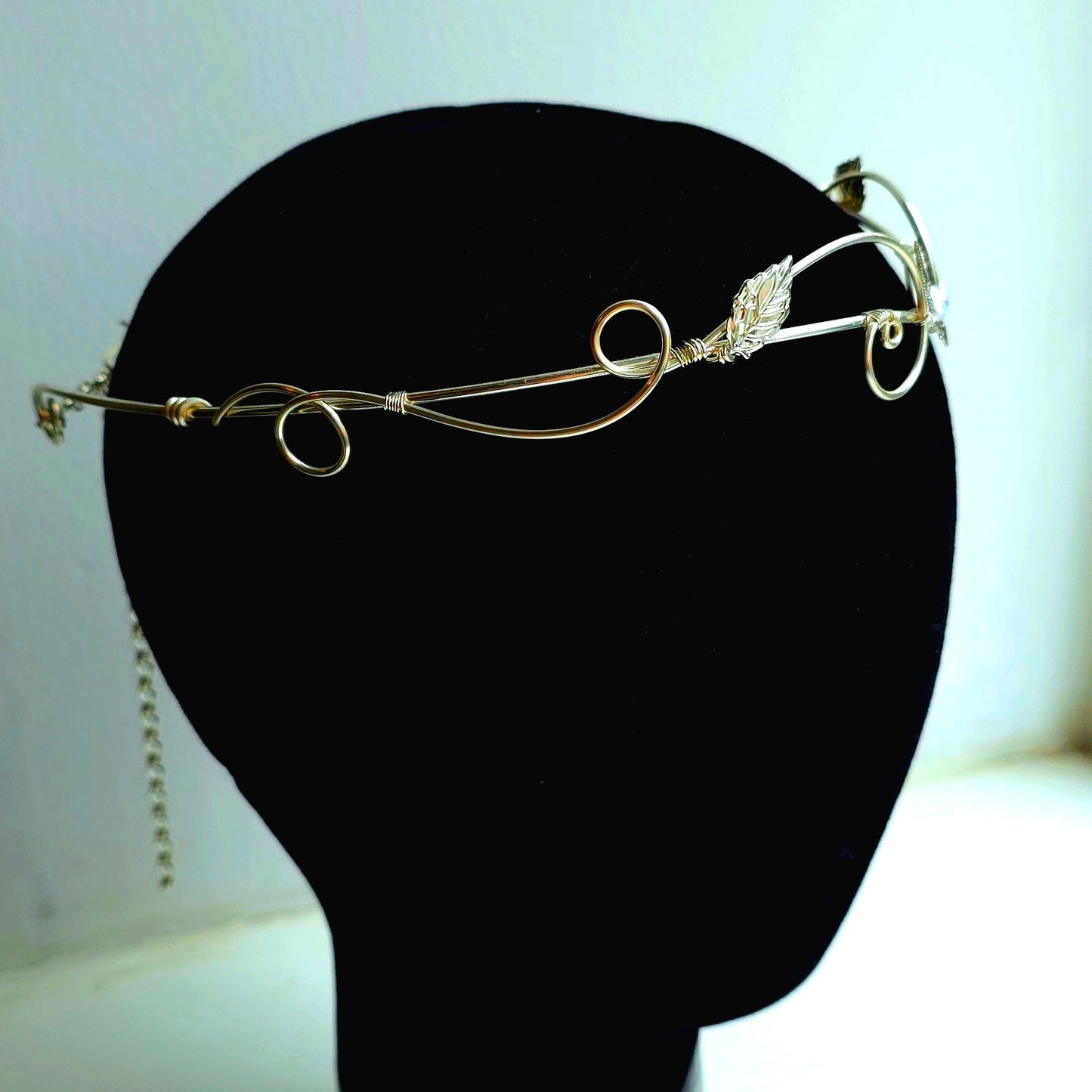 A delicate silver wire filigree headband with a small clear crystal accent, displayed on a black mannequin head against a light background.
