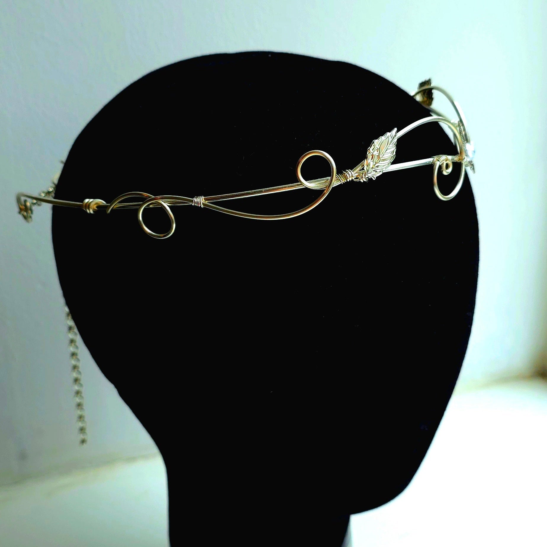 A delicate silver wire filigree headband with a small clear crystal accent, displayed on a black mannequin head against a light background.