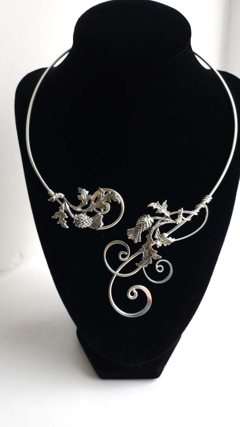 Silver necklace with intricate designs on a black bust against a white background