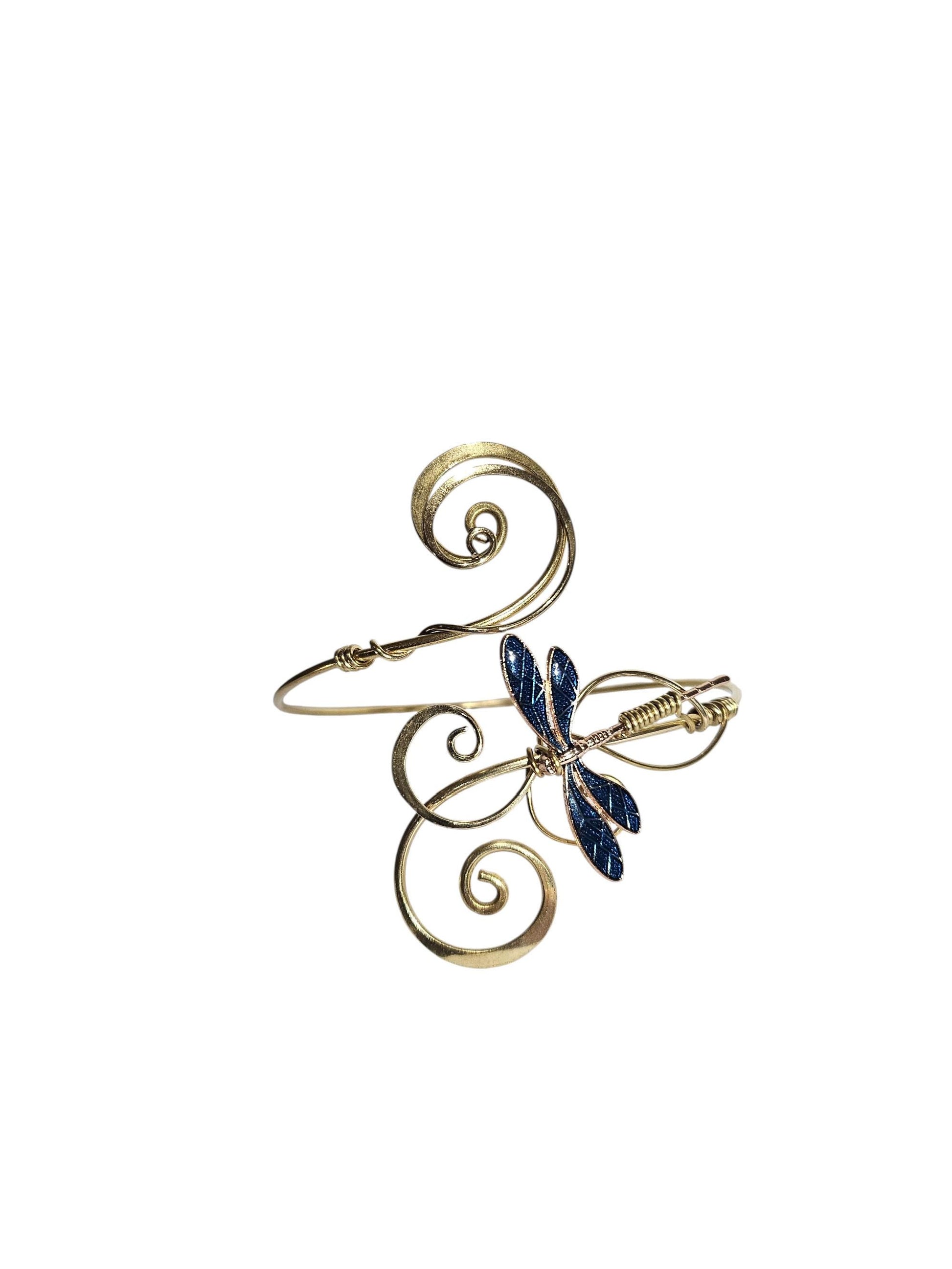 Product studio shot of a gold-tone brass wire dragonfly arm cuff featuring scrolled filigree details and dark blue textured wings, isolated on a white background.