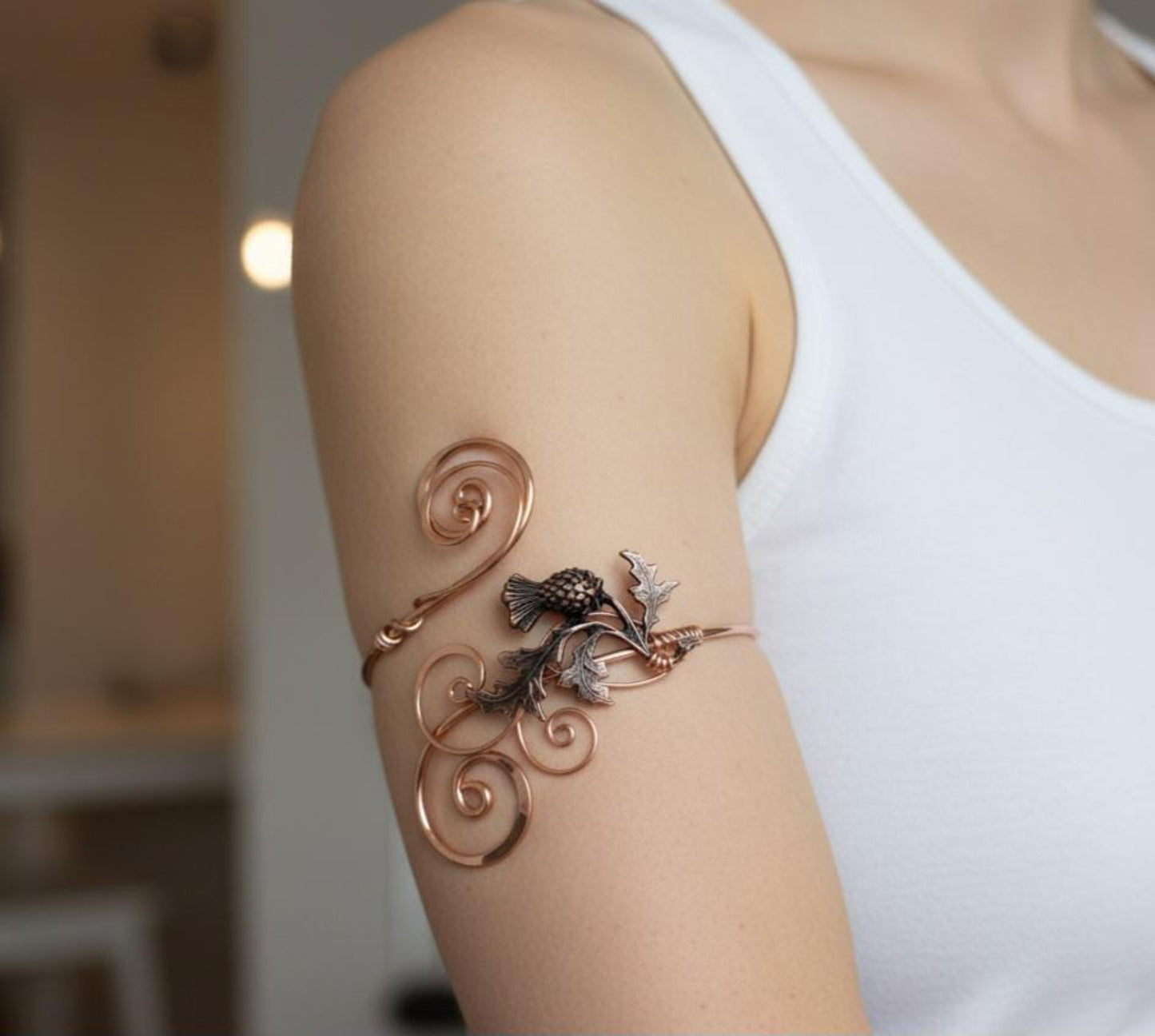 Handcrafted copper thistle arm cuff shown worn on a woman's upper arm, featuring a detailed Scottish thistle motif and hand-hammered organic wire curls.
