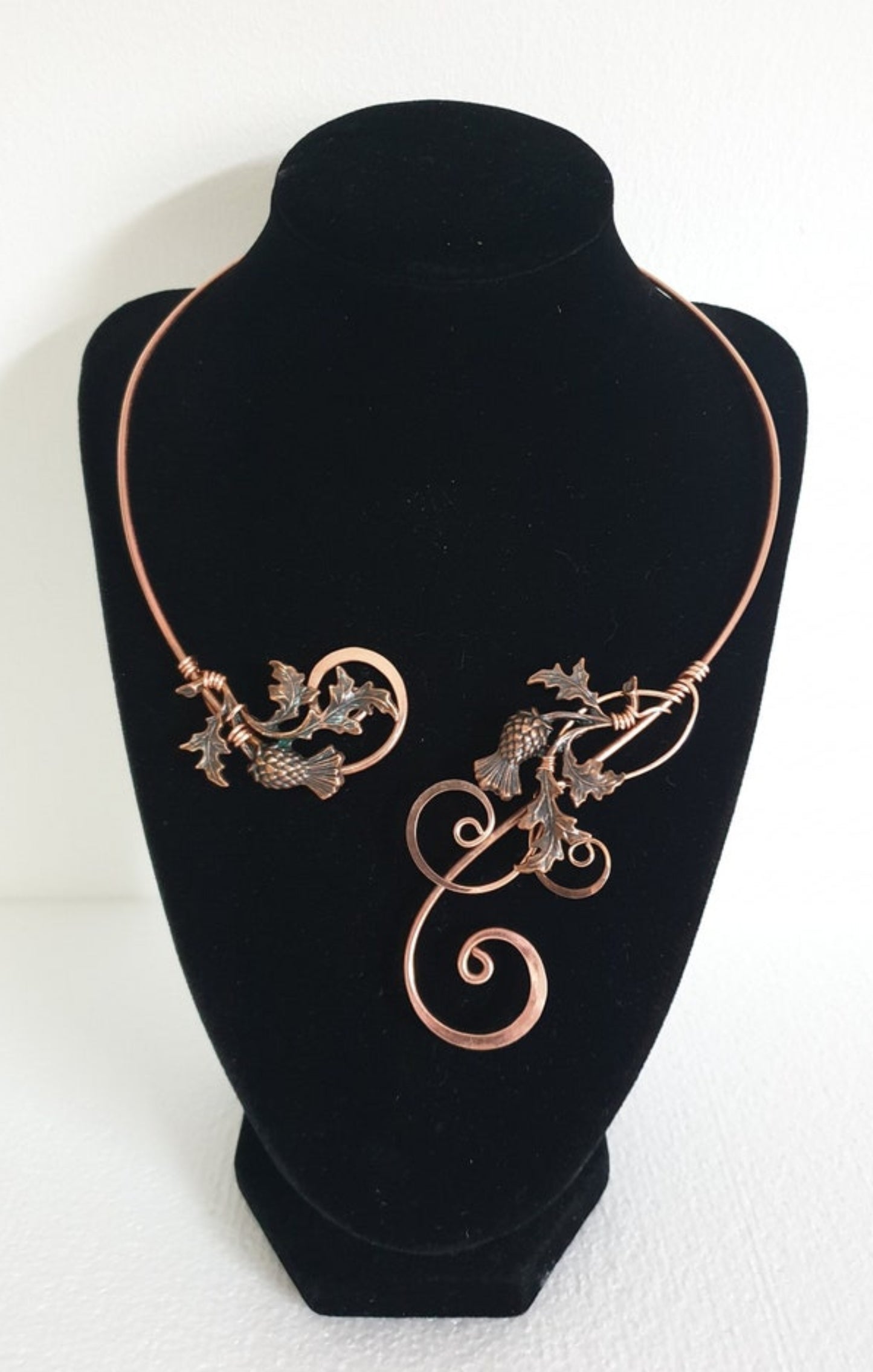 Handcrafted hammered copper thistle torc necklace displayed on a black velvet neck form, showing the intricate wire-woven Scottish thistle design.