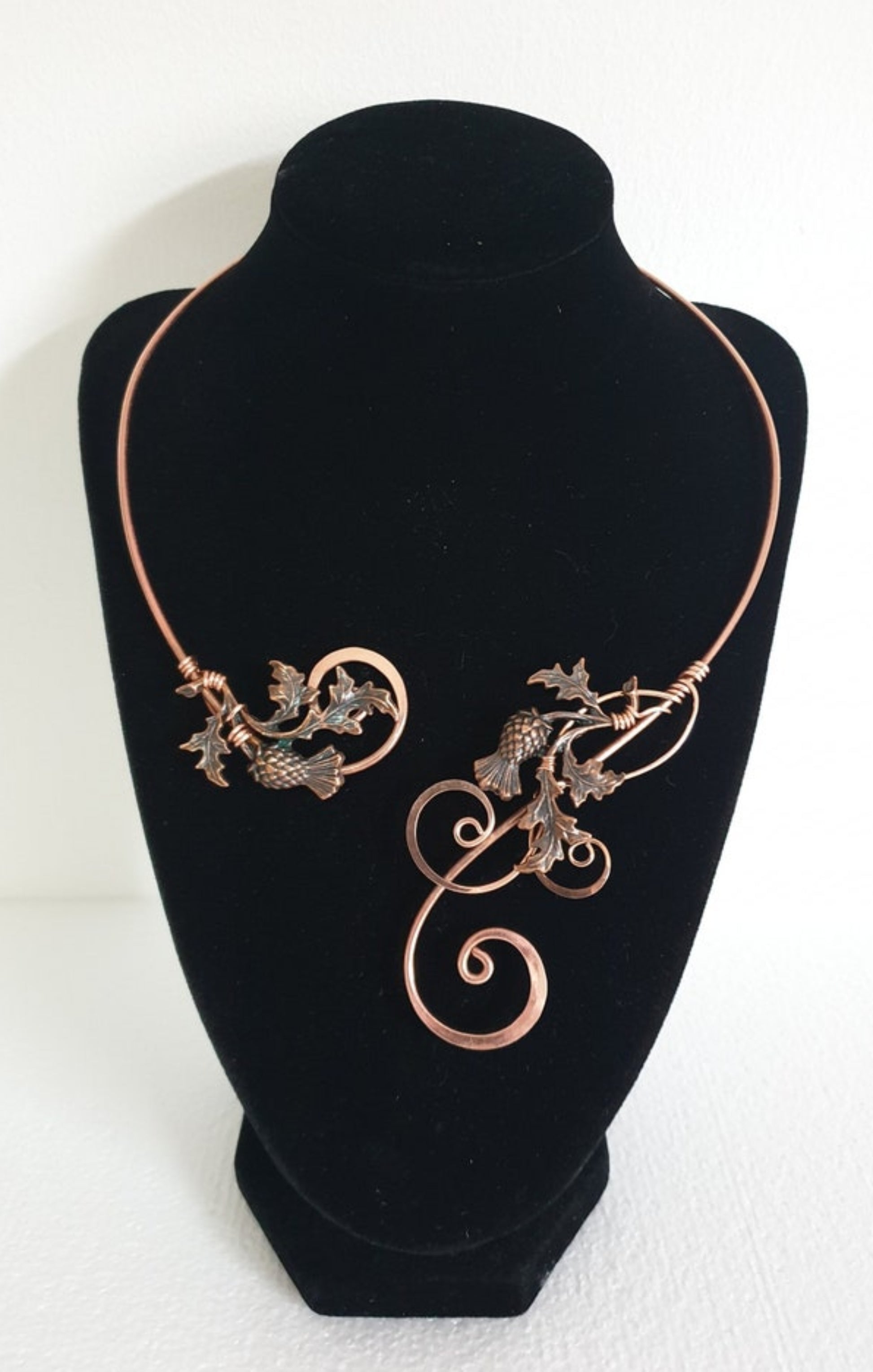 Handcrafted hammered copper thistle torc necklace displayed on a black velvet neck form, showing the intricate wire-woven Scottish thistle design.