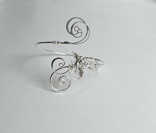 Handcrafted silver wire-wrapped arm cuff featuring a detailed honeybee charm and elegant swirling scrollwork on a light background.