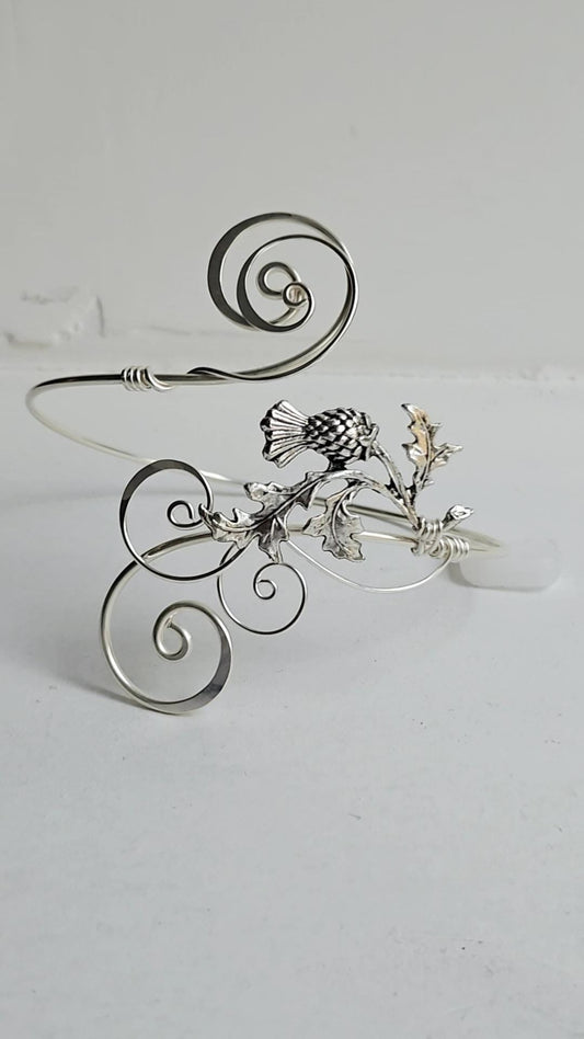 Handcrafted silver-plated thistle arm cuff featuring an intricate wire-wrapped scroll design and a detailed thistle charm on a light background.